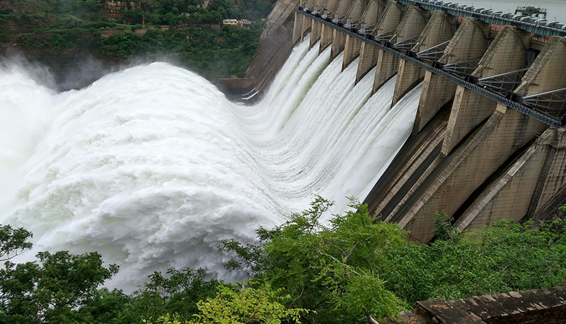 A rushing dam with white water and greenery surrounding it.