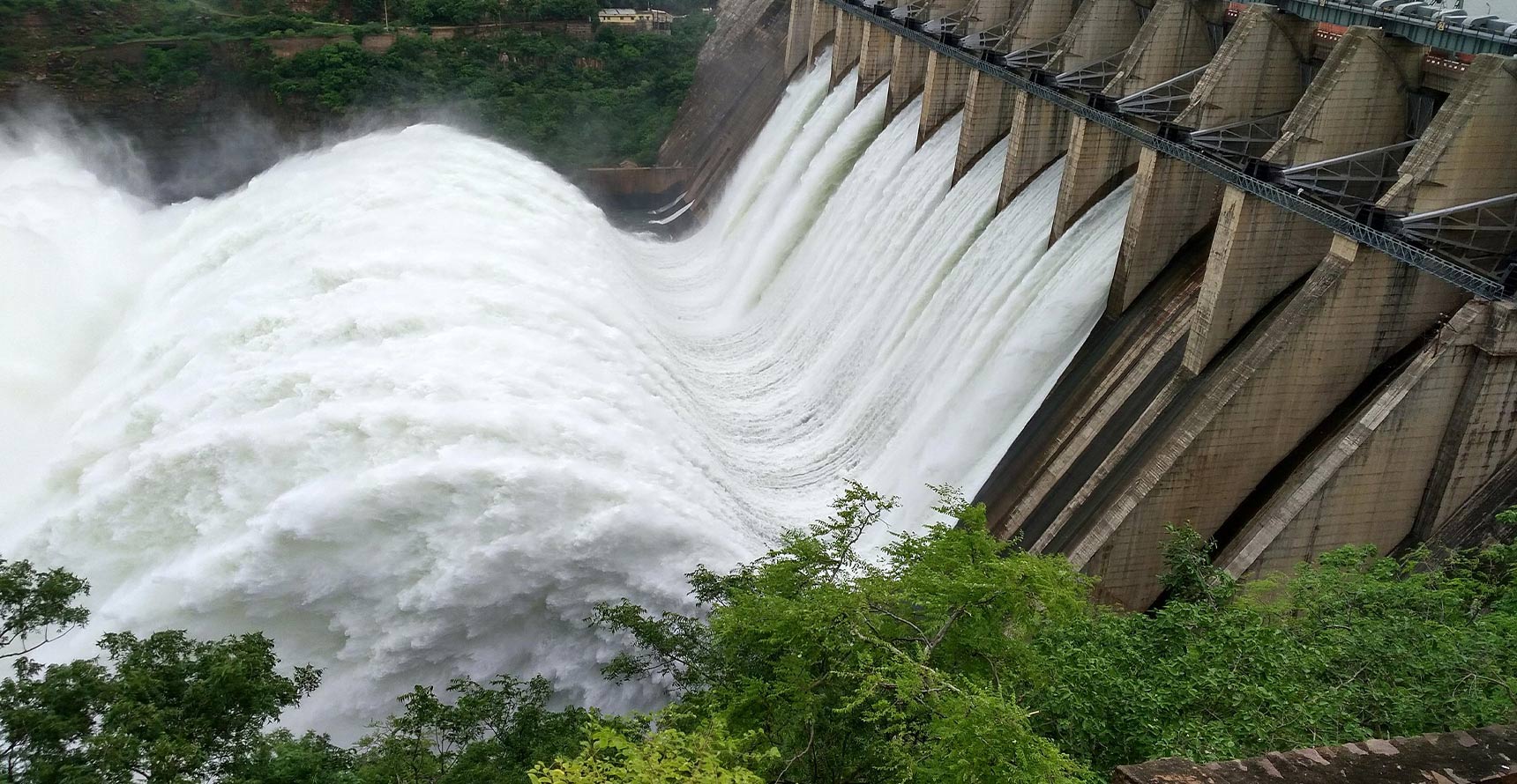 A dam with rushing white water with greenery around it.