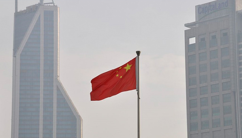 Chinese flag flying in foreground. High-rise buildings in background.