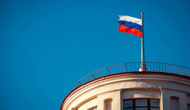 Photo of a Russian flag flying above a building in front of a blue sky