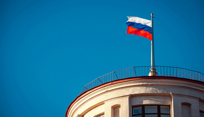 Photo of a Russian flag flying above a building in front of a blue sky